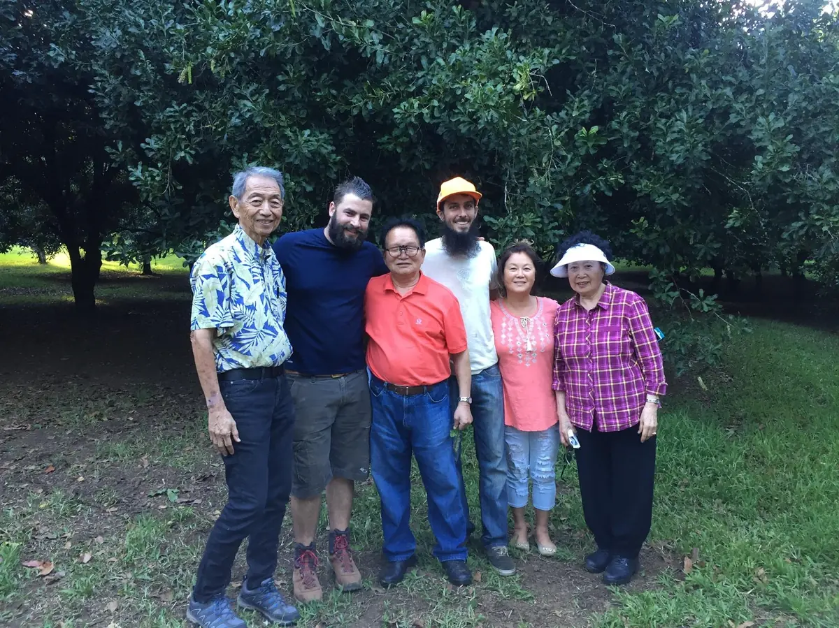 Master Cho Han-kyu in a red shirt standing with six Hawaiʻi growers in an orchard